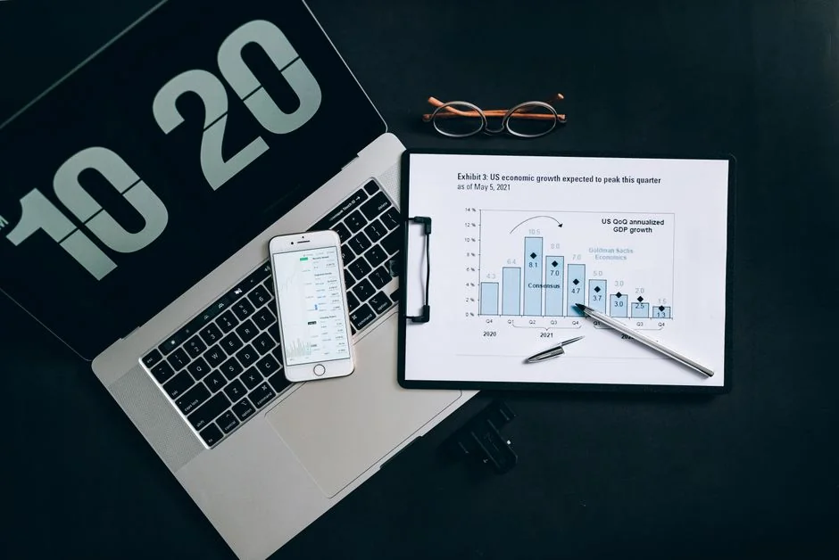 Man analyzing stock trends with laptop and mobile trading app at a modern workspace.